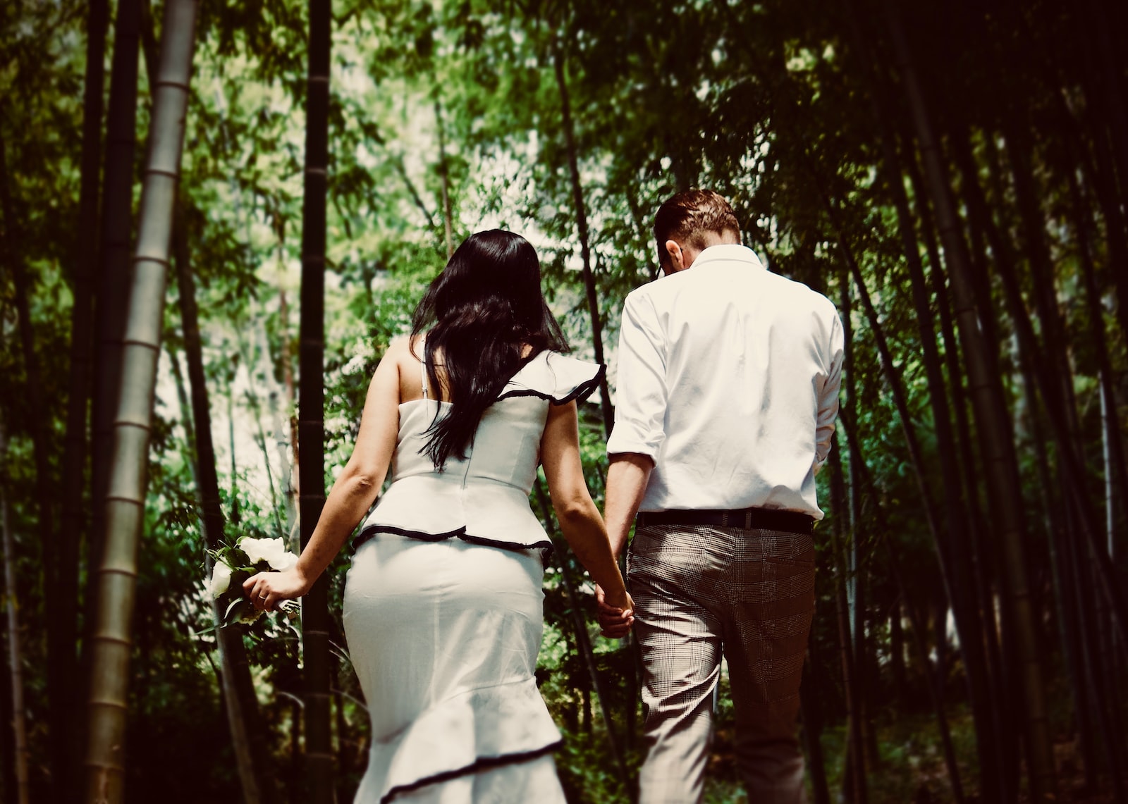 man and woman holding hands while walking near trees